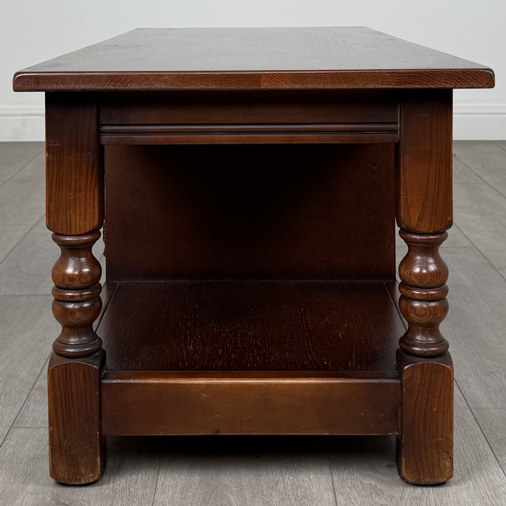 A low rectangular warm brown oak coffee table featuring turned baluster legs, a lower shelf, and a central cupboard door decorated with carved linenfold panelling. View IV