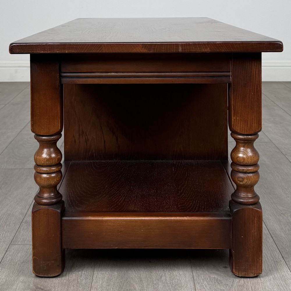 A low rectangular warm brown oak coffee table featuring turned baluster legs, a lower shelf, and a central cupboard door decorated with carved linenfold panelling. View VIII