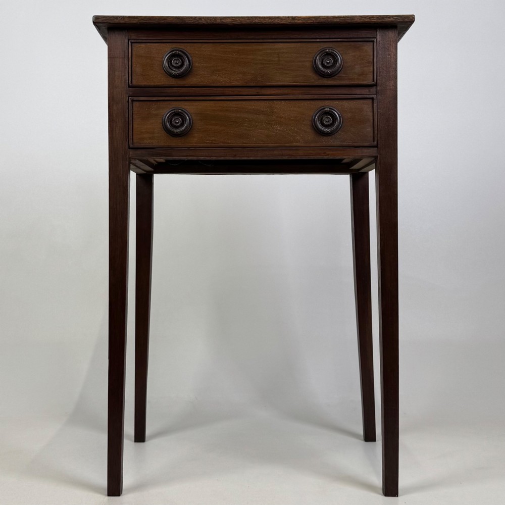 An antique dark mahogany side table featuring two stacked drawers with circular handles, supported by tall tapered square legs.