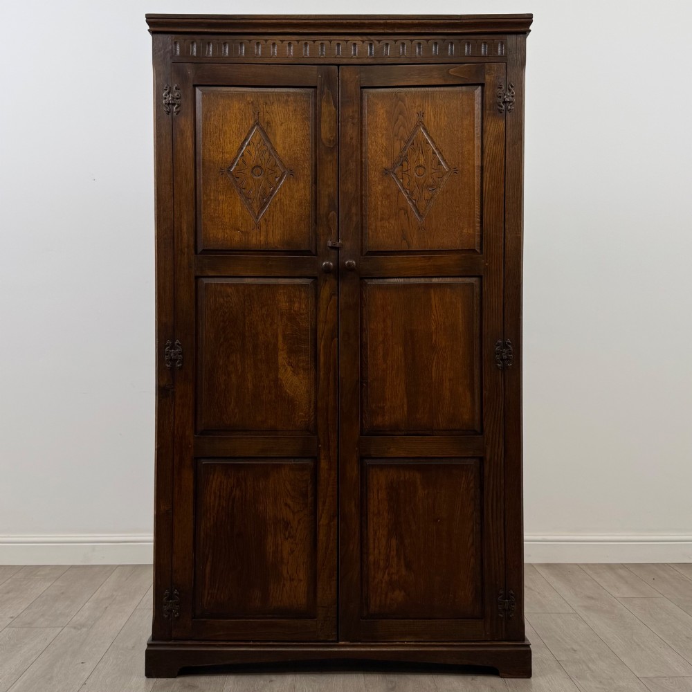 A tall dark oak Edwardian two-door wardrobe featuring carved diamond panel details and decorative iron hinges.