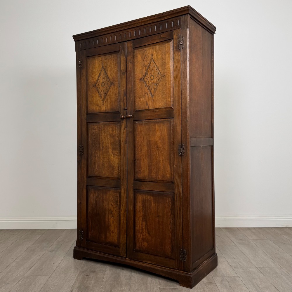 A tall dark oak Edwardian two-door wardrobe featuring carved diamond panel details and decorative iron hinges. View III