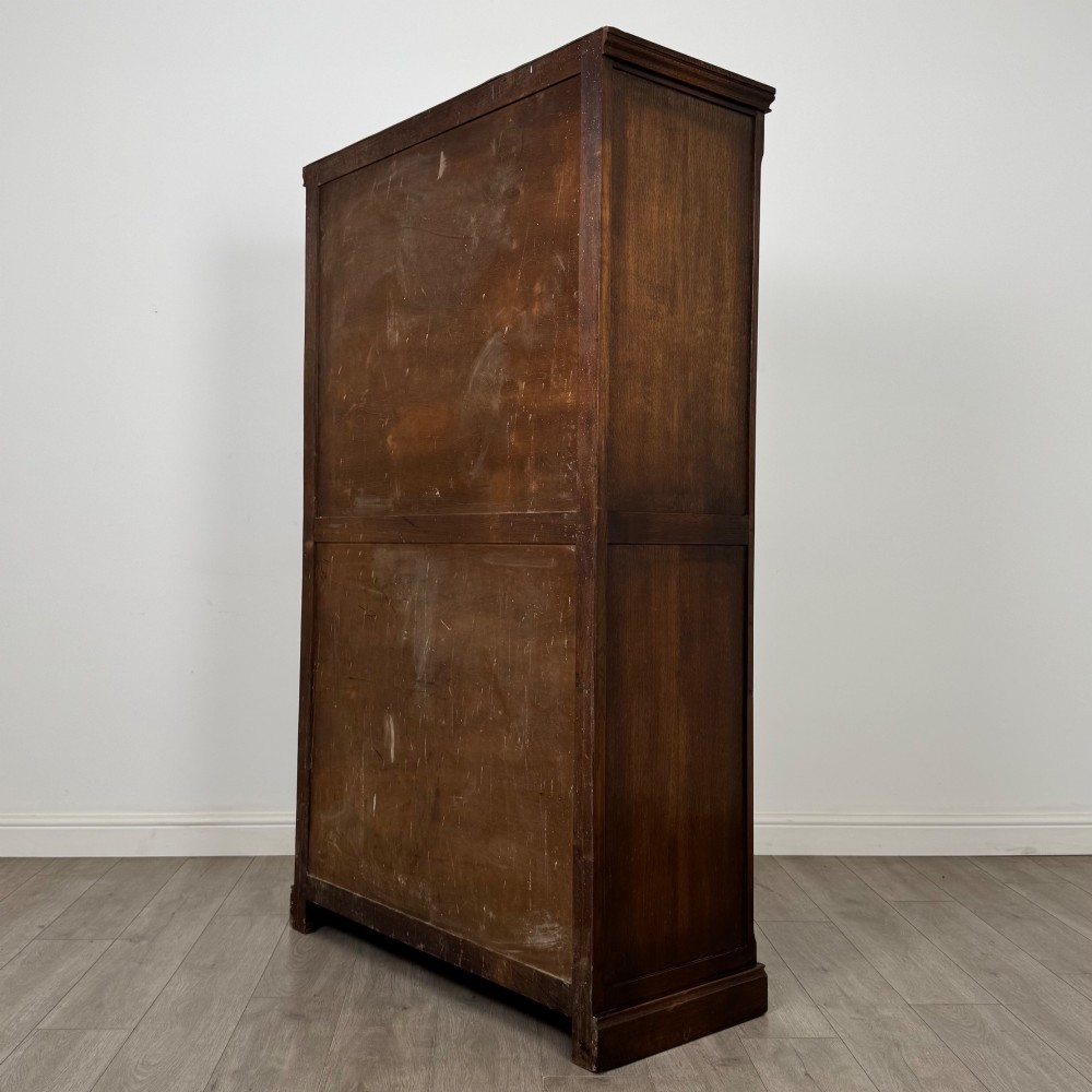 A tall dark oak Edwardian two-door wardrobe featuring carved diamond panel details and decorative iron hinges. View VII