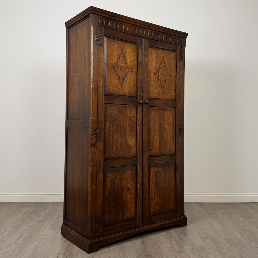 A tall dark oak Edwardian two-door wardrobe featuring carved diamond panel details and decorative iron hinges. View IX