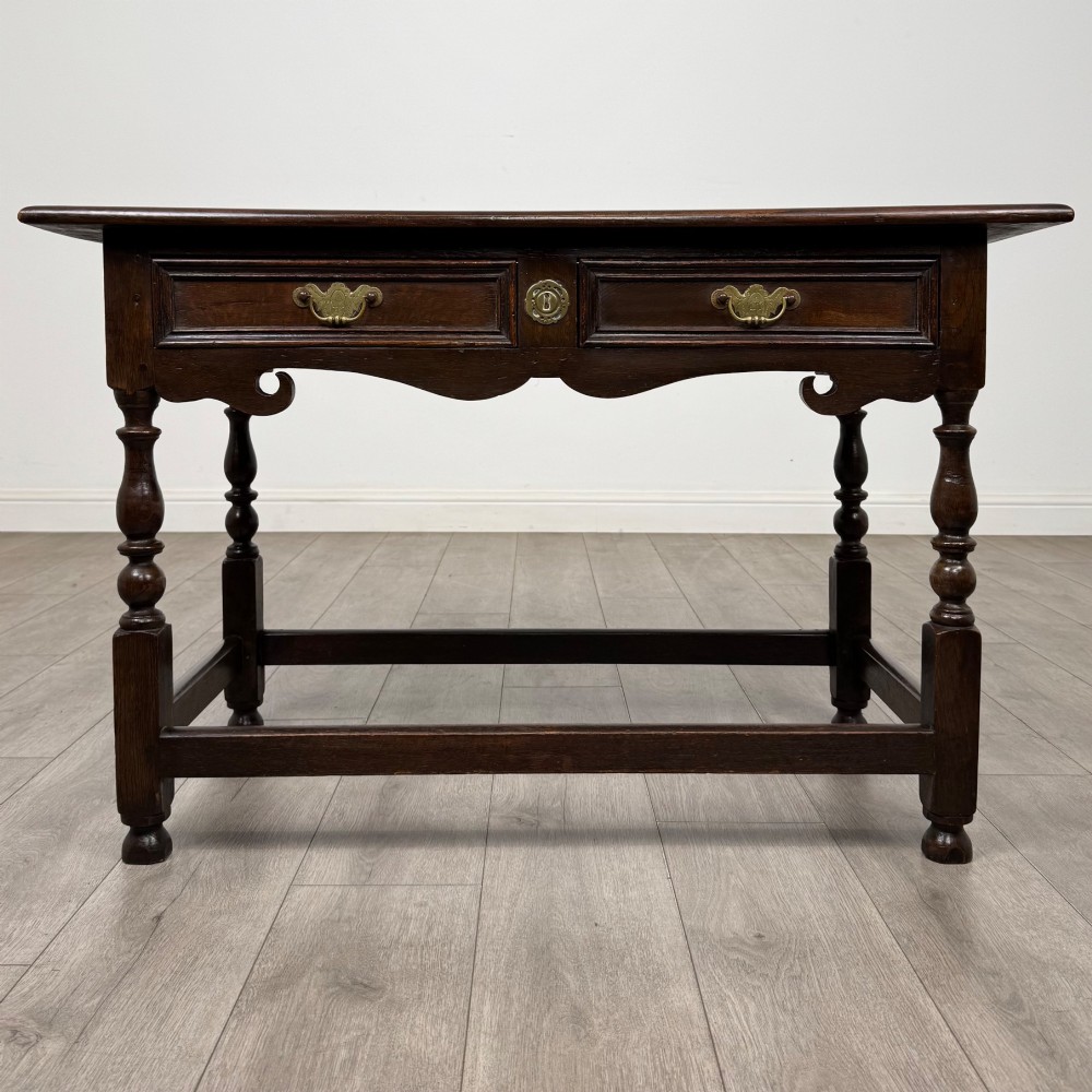 An 18th-century dark oak Georgian side table featuring two frieze drawers with brass handles, turned legs, a shaped apron, and a lower box stretcher.