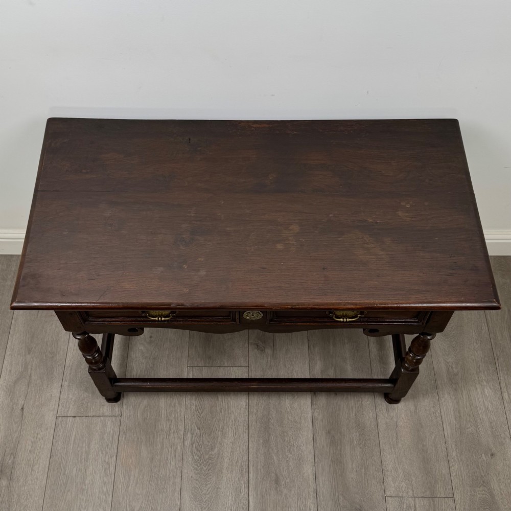 An 18th-century dark oak Georgian side table featuring two frieze drawers with brass handles, turned legs, a shaped apron, and a lower box stretcher. View IX
