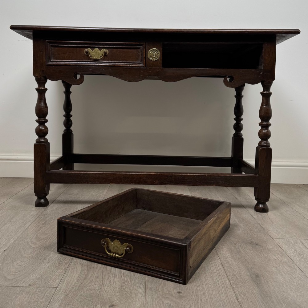 An 18th-century dark oak Georgian side table featuring two frieze drawers with brass handles, turned legs, a shaped apron, and a lower box stretcher. View X