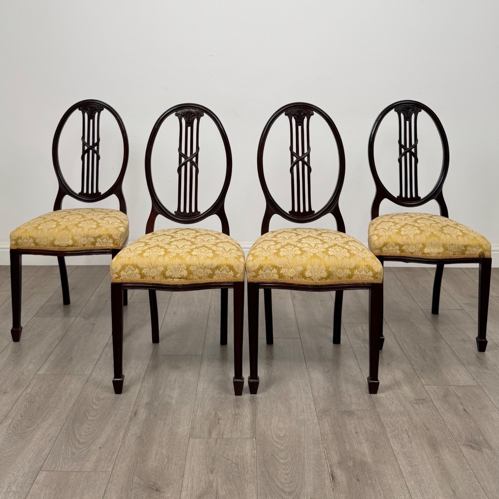 A set of four dark mahogany dining chairs with carved oval backs, slender vertical splats, and gold damask upholstered seats.