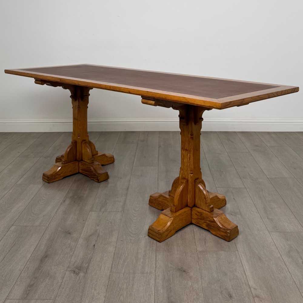 A large twentieth-century Arts and Crafts oak library table with an inset brown leather writing top resting on dual pedestal trestle supports.