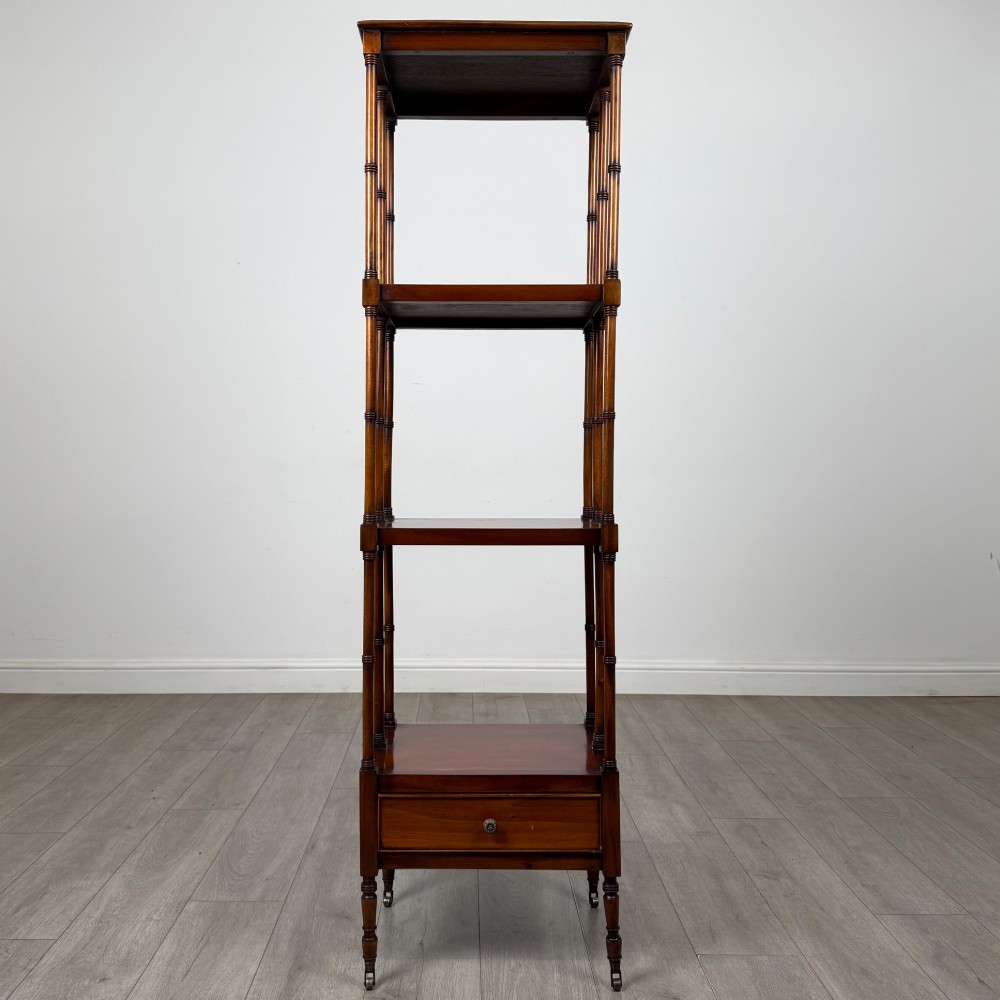 A tall, narrow 20th-century mahogany open bookcase featuring four tiered shelves supported by turned columns and a single drawer at the base raised on brass castors.