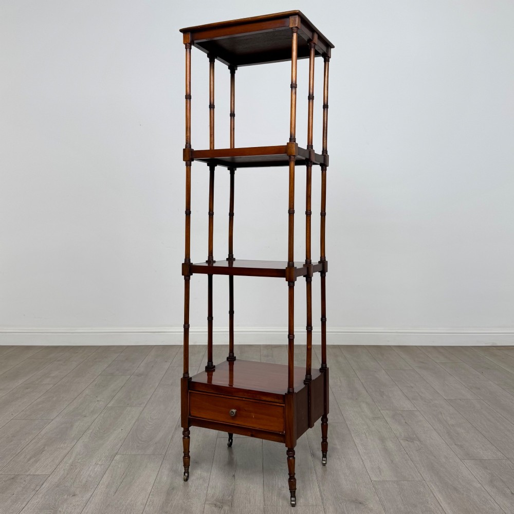 A tall, narrow 20th-century mahogany open bookcase featuring four tiered shelves supported by turned columns and a single drawer at the base raised on brass castors. View II
