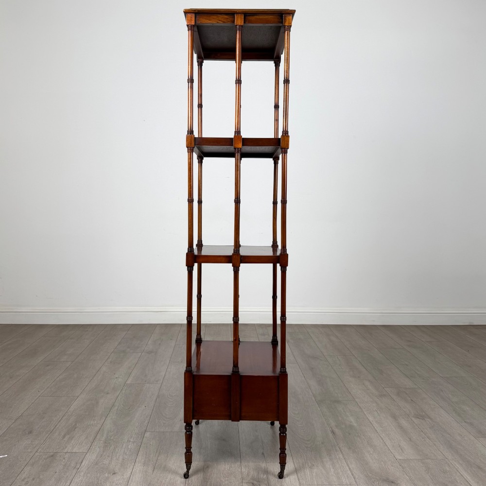 A tall, narrow 20th-century mahogany open bookcase featuring four tiered shelves supported by turned columns and a single drawer at the base raised on brass castors. View III