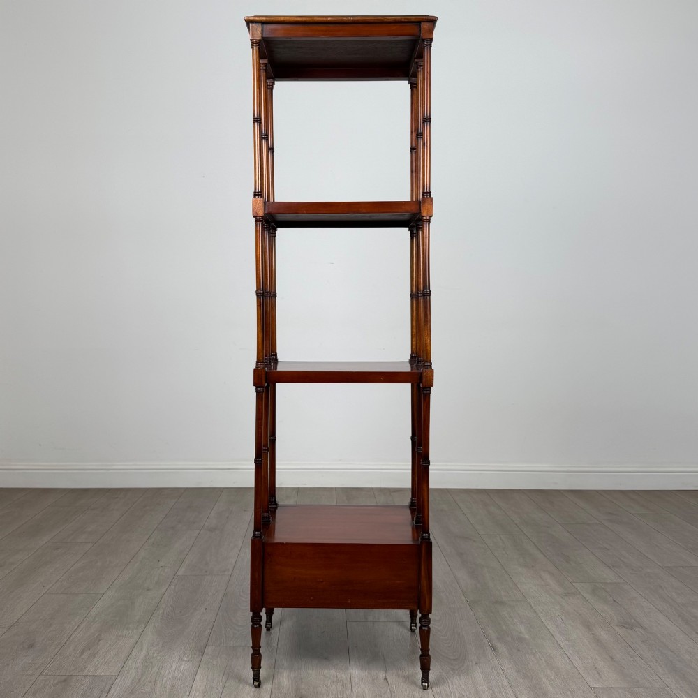 A tall, narrow 20th-century mahogany open bookcase featuring four tiered shelves supported by turned columns and a single drawer at the base raised on brass castors. View V
