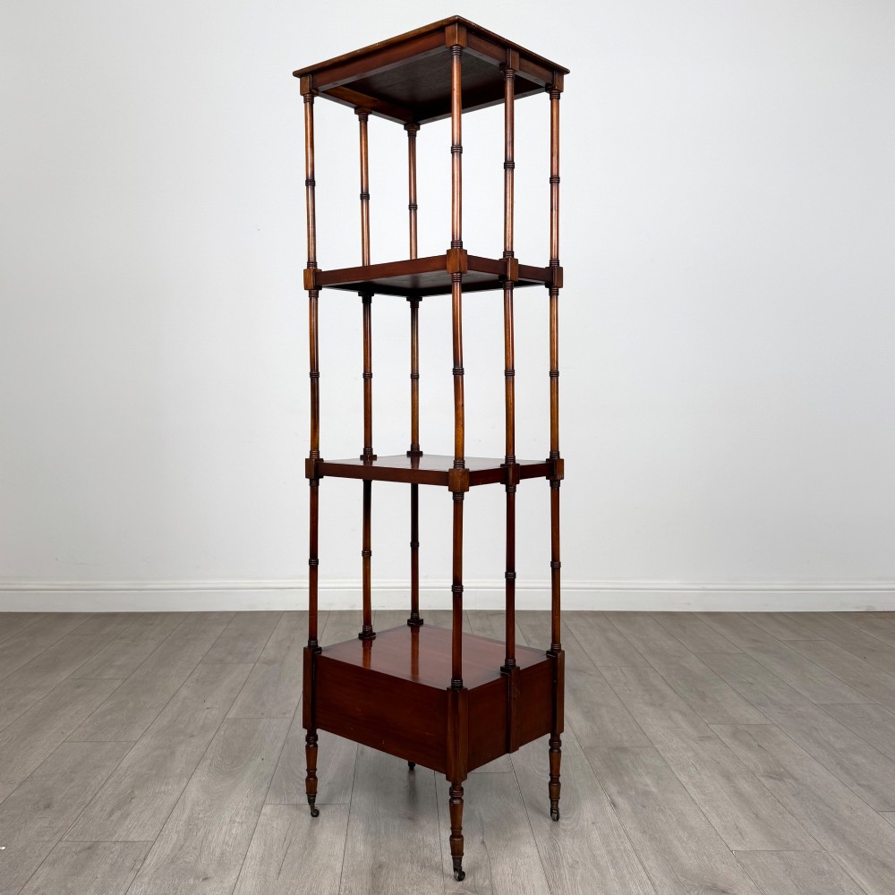 A tall, narrow 20th-century mahogany open bookcase featuring four tiered shelves supported by turned columns and a single drawer at the base raised on brass castors. View VI