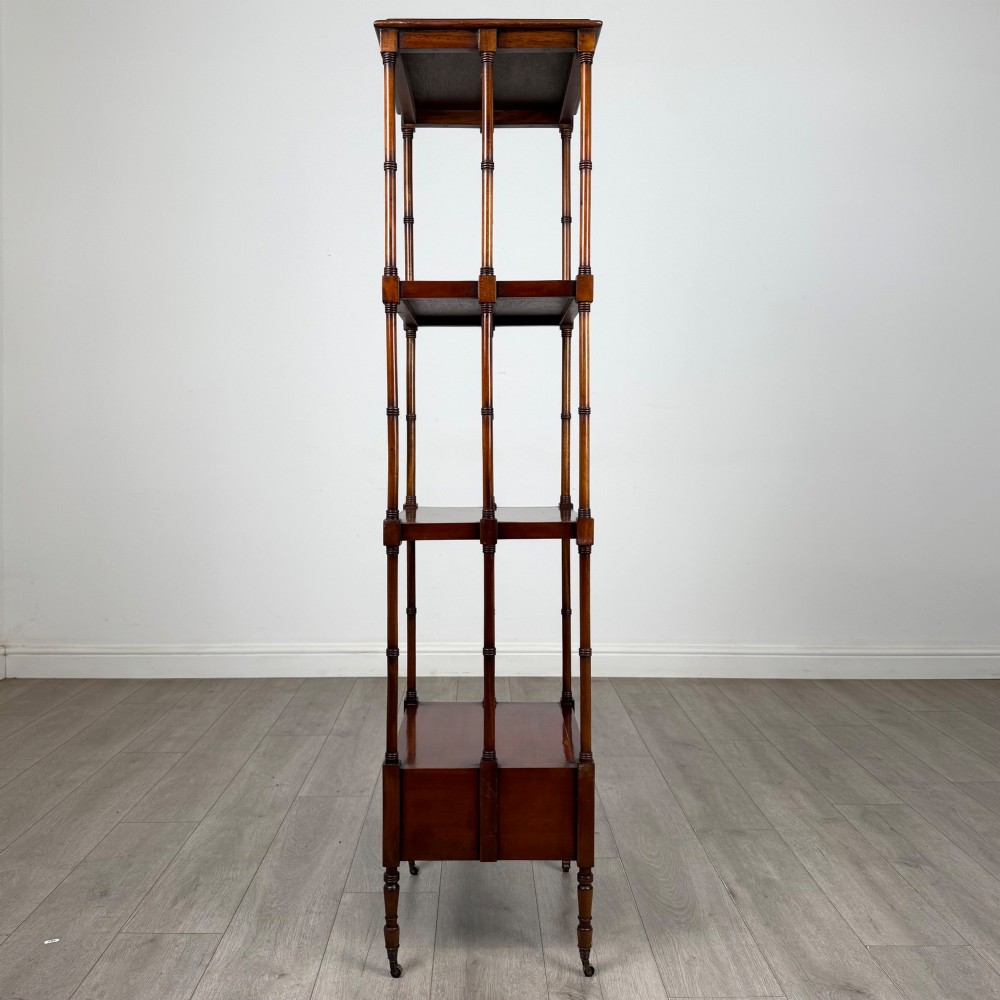 A tall, narrow 20th-century mahogany open bookcase featuring four tiered shelves supported by turned columns and a single drawer at the base raised on brass castors. View VII