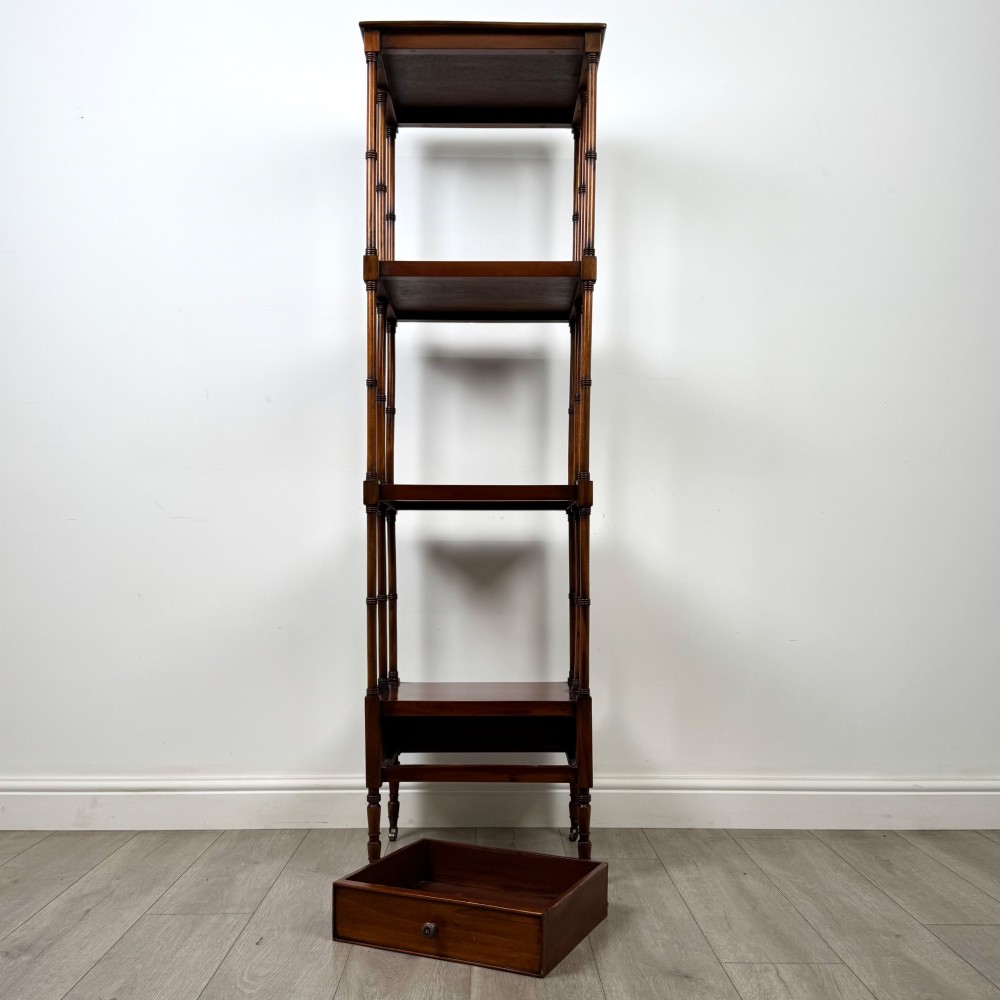 A tall, narrow 20th-century mahogany open bookcase featuring four tiered shelves supported by turned columns and a single drawer at the base raised on brass castors. View IX