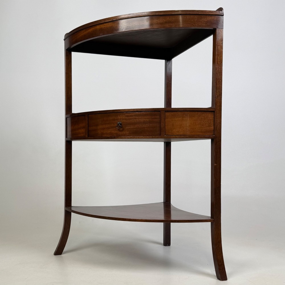 A three-tiered Georgian style mahogany corner stand featuring a curved front, single drawer with brass ring pull, and splayed legs. View II