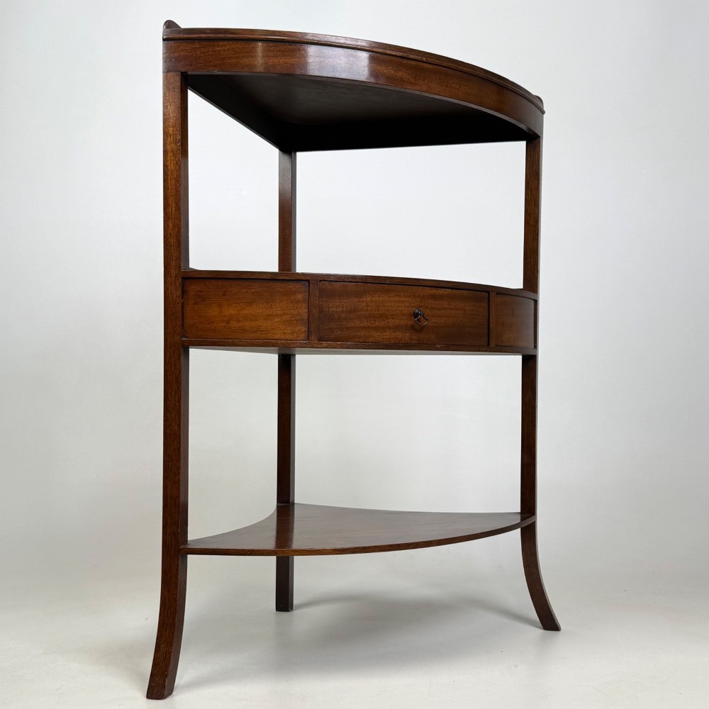 A three-tiered Georgian style mahogany corner stand featuring a curved front, single drawer with brass ring pull, and splayed legs. View IV