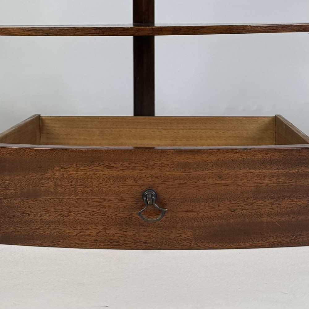 A three-tiered Georgian style mahogany corner stand featuring a curved front, single drawer with brass ring pull, and splayed legs. View VII