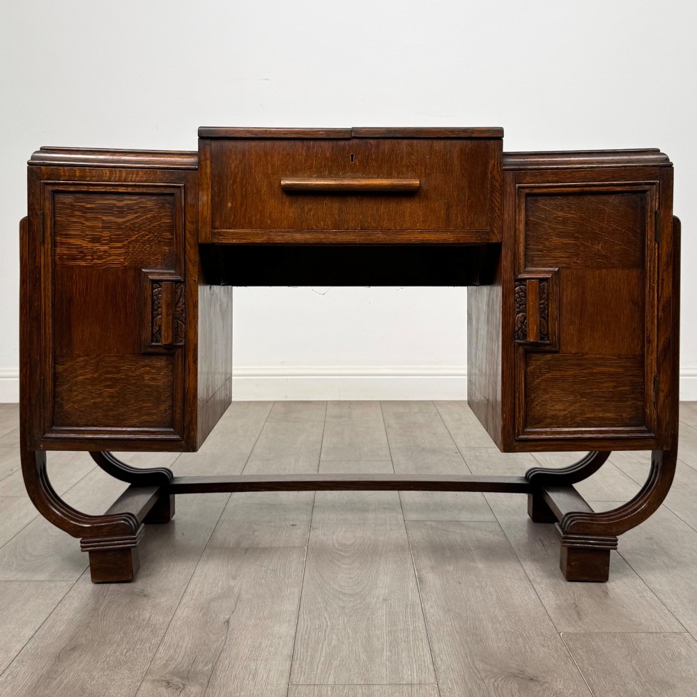 An Art Deco oak desk featuring two side cupboard pedestals supported by u-shaped curved legs and a central drawer.