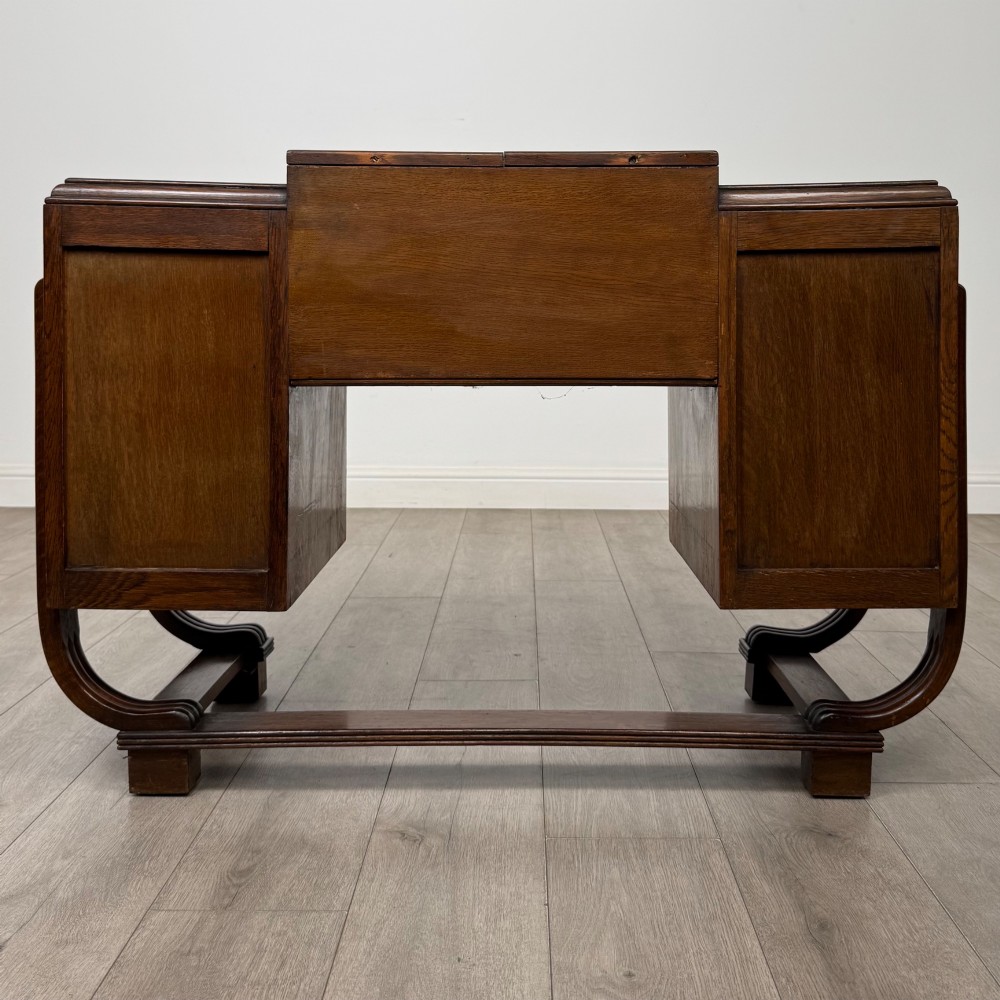 An Art Deco oak desk featuring two side cupboard pedestals supported by u-shaped curved legs and a central drawer. View VI