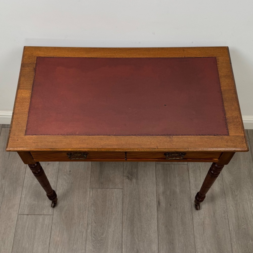 A 19th-century Victorian golden oak writing table featuring a single frieze drawer with decorative brass handles and ring-turned legs on castors. View IX