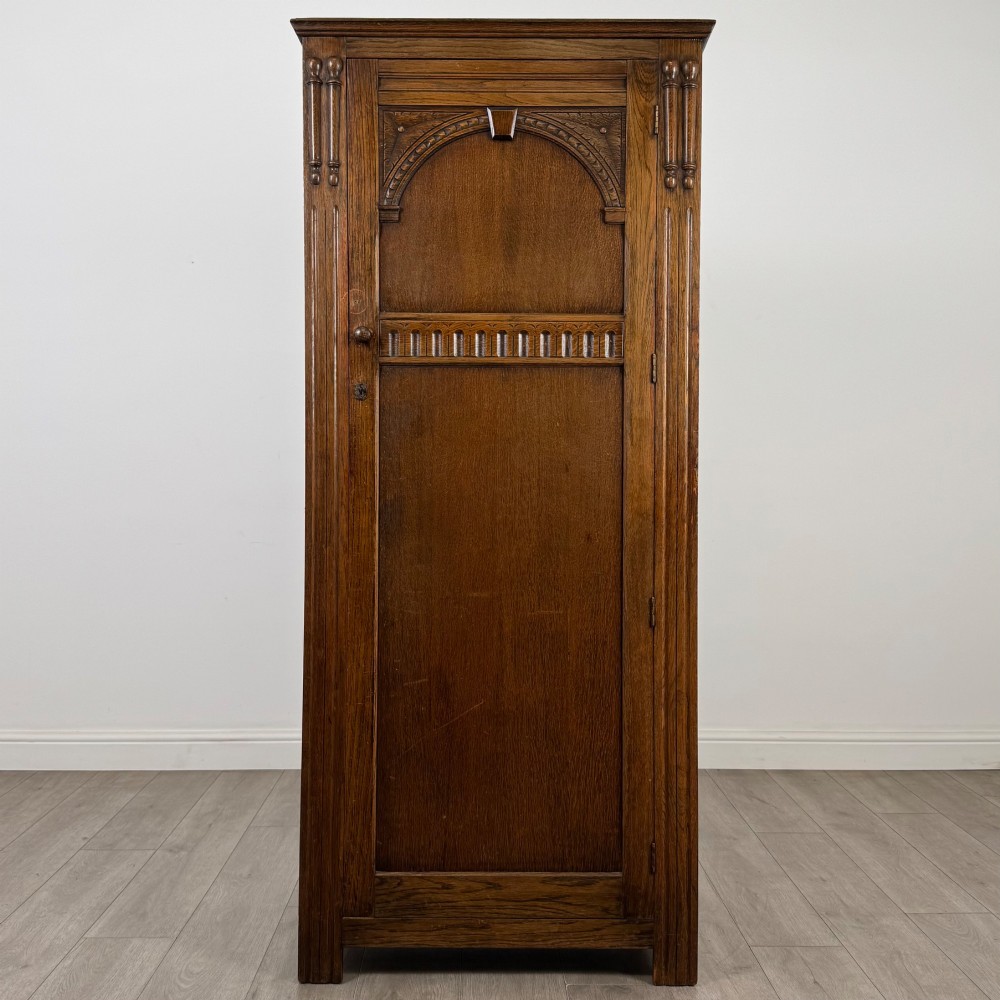 A tall, single-door Edwardian oak wardrobe featuring carved arched upper panelling and turned side columns.