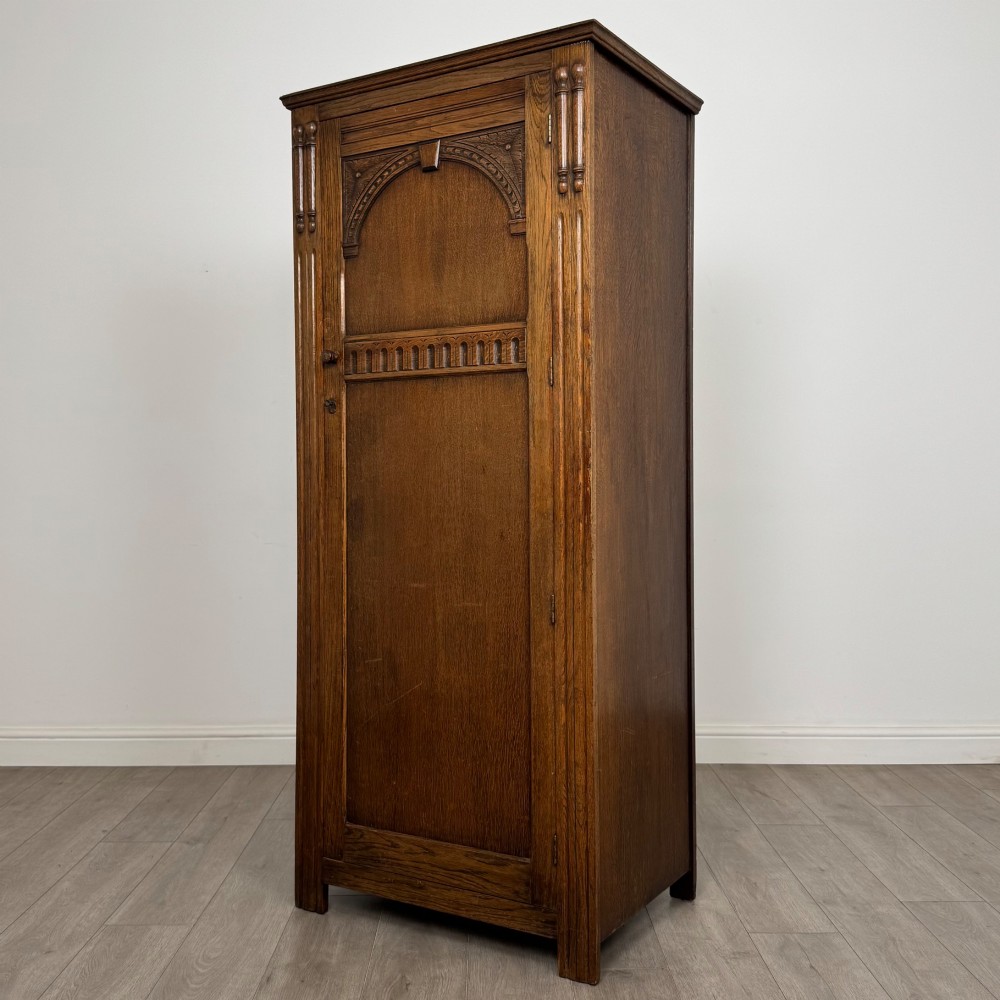 A tall, single-door Edwardian oak wardrobe featuring carved arched upper panelling and turned side columns. View III