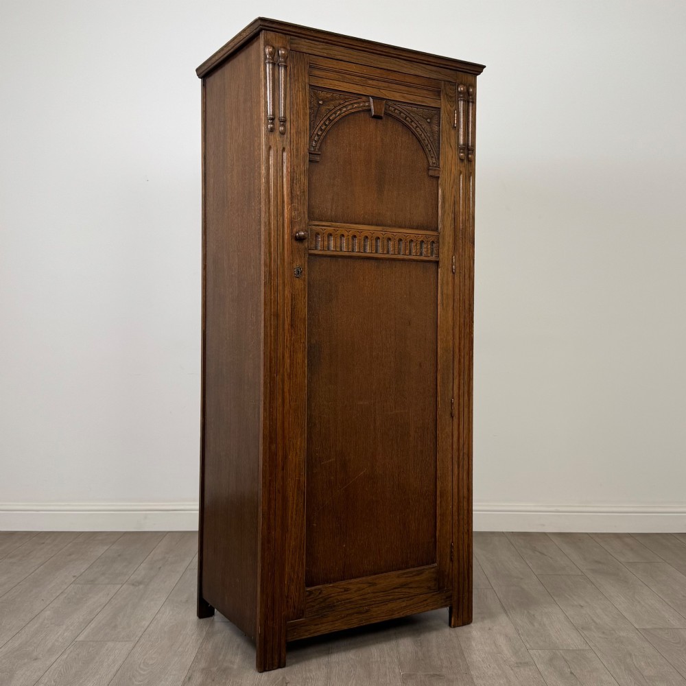 A tall, single-door Edwardian oak wardrobe featuring carved arched upper panelling and turned side columns. View IX