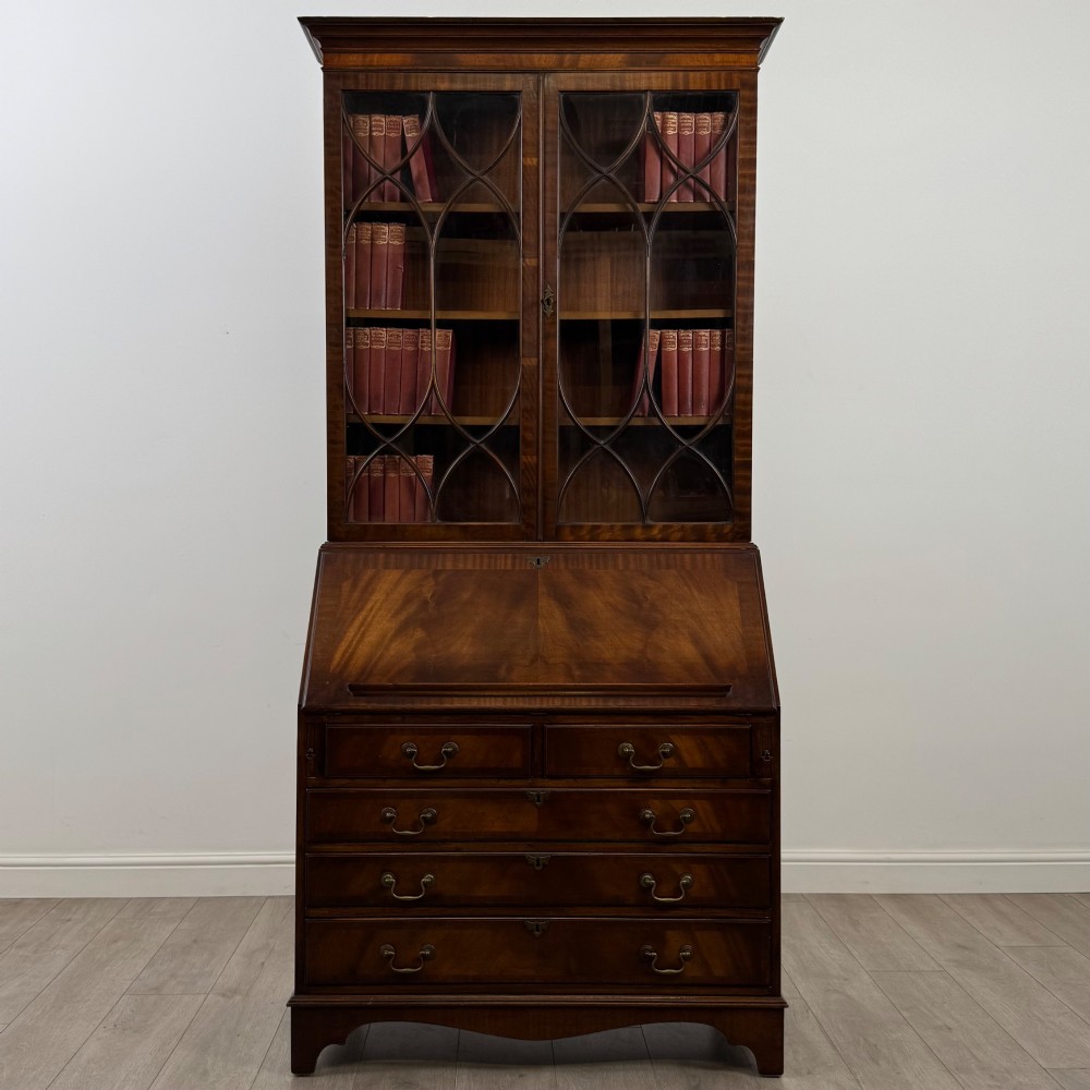 An antique mahogany bureau bookcase featuring two astragal glazed glass upper doors above a lower drop-front writing slope and four drawers.