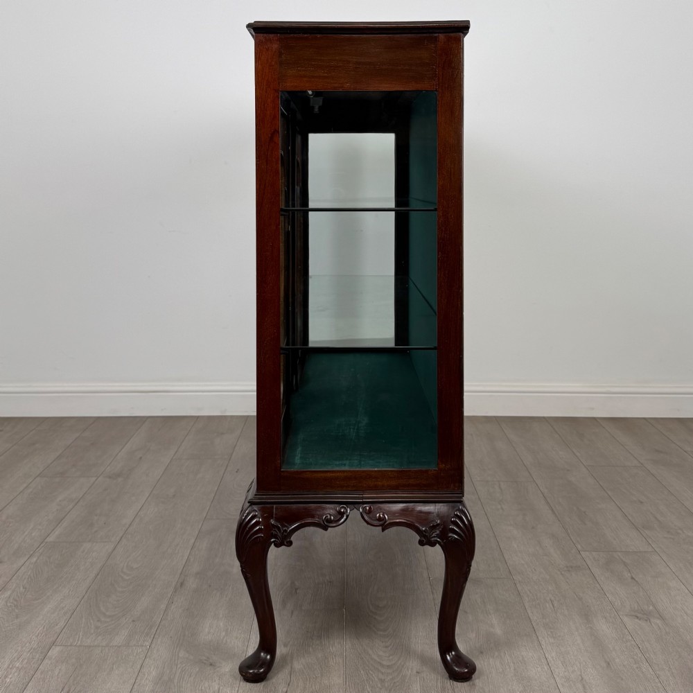 An early twentieth-century mahogany display cabinet featuring three glazed doors with curved astragal glazing bars, a carved top frieze, green fabric interior, and cabriole legs. View IV