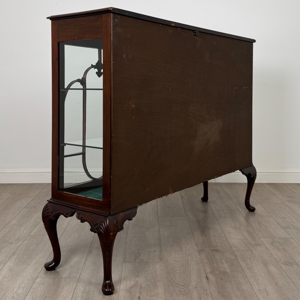 An early twentieth-century mahogany display cabinet featuring three glazed doors with curved astragal glazing bars, a carved top frieze, green fabric interior, and cabriole legs. View V