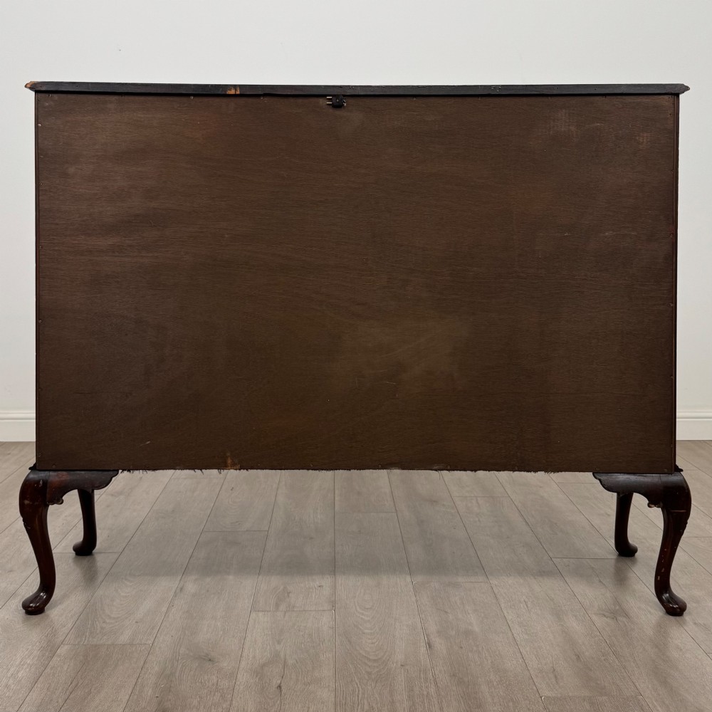 An early twentieth-century mahogany display cabinet featuring three glazed doors with curved astragal glazing bars, a carved top frieze, green fabric interior, and cabriole legs. View VI