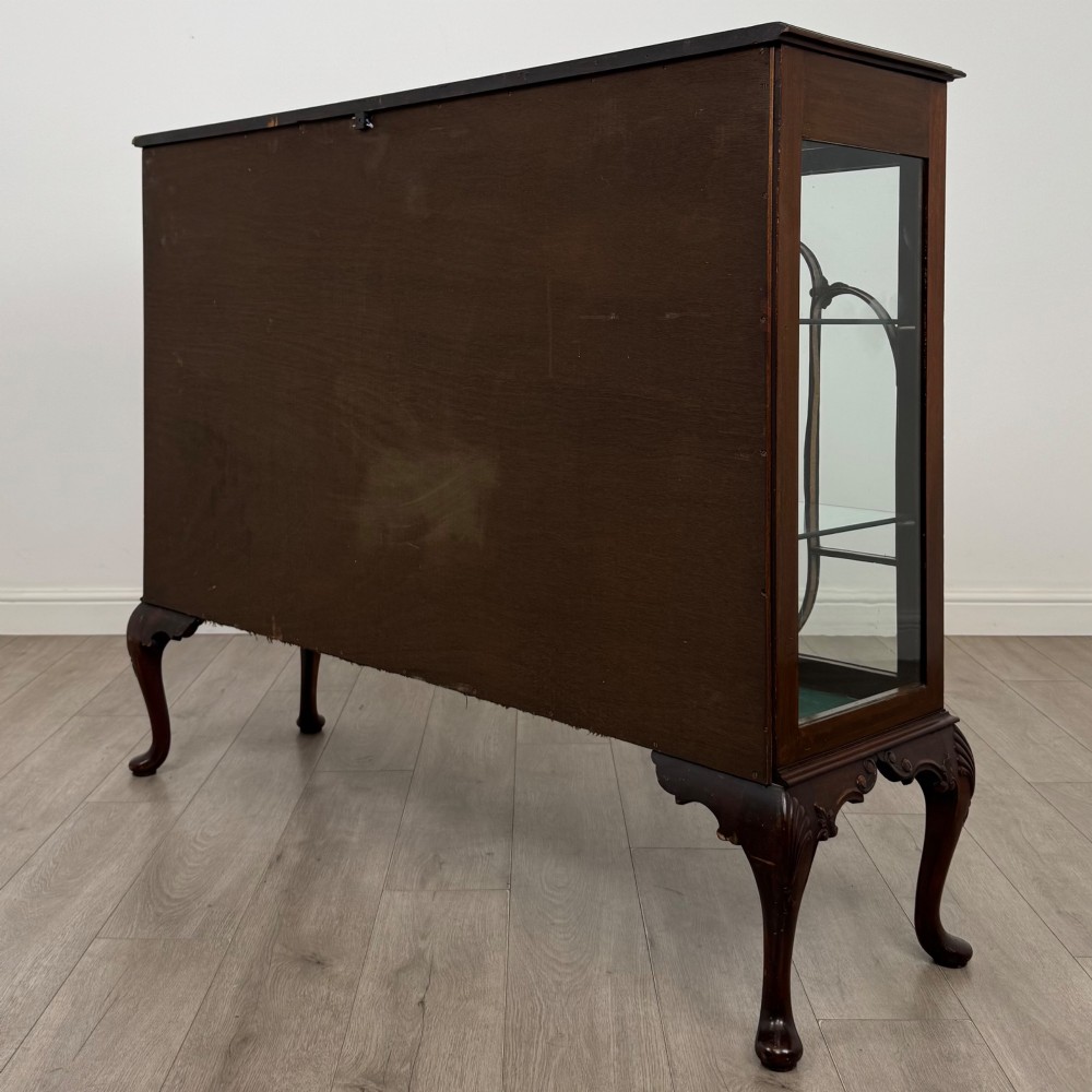 An early twentieth-century mahogany display cabinet featuring three glazed doors with curved astragal glazing bars, a carved top frieze, green fabric interior, and cabriole legs. View VII