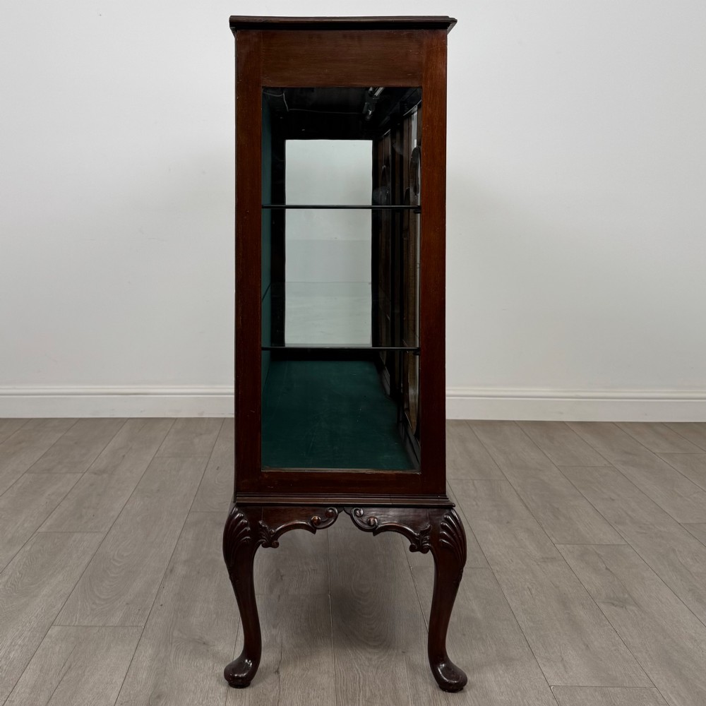 An early twentieth-century mahogany display cabinet featuring three glazed doors with curved astragal glazing bars, a carved top frieze, green fabric interior, and cabriole legs. View VIII