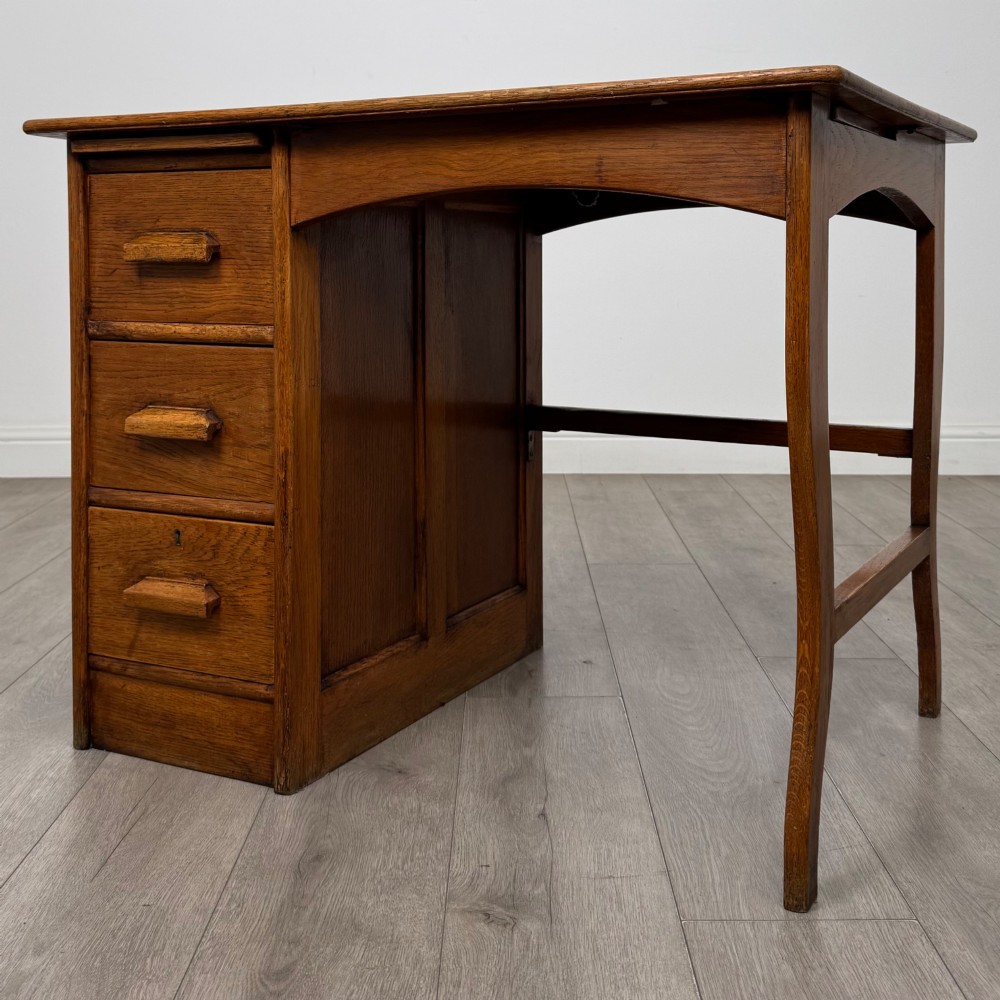 An Edwardian single pedestal oak desk with three stacked drawers on the left, integrated wood pulls, and an open kneehole section supported by slim right-side legs. View II