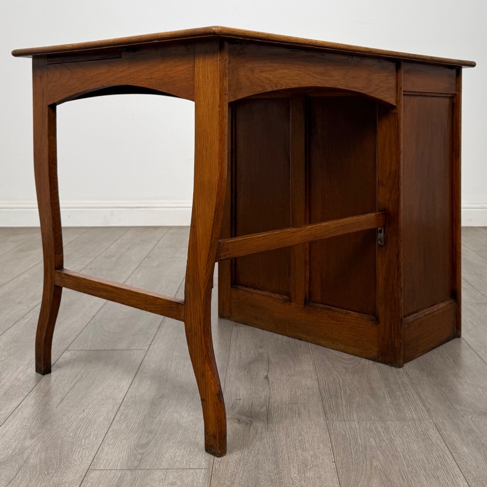 An Edwardian single pedestal oak desk with three stacked drawers on the left, integrated wood pulls, and an open kneehole section supported by slim right-side legs. View IV