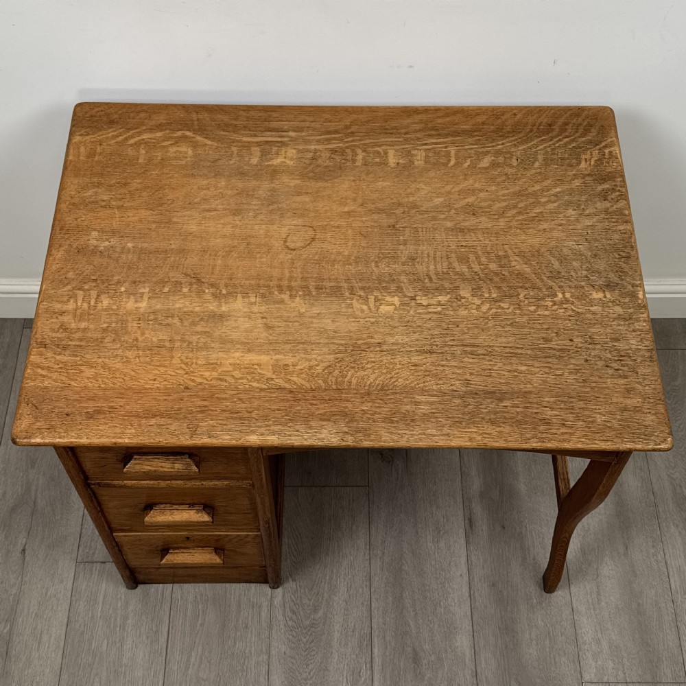 An Edwardian single pedestal oak desk with three stacked drawers on the left, integrated wood pulls, and an open kneehole section supported by slim right-side legs. View IX