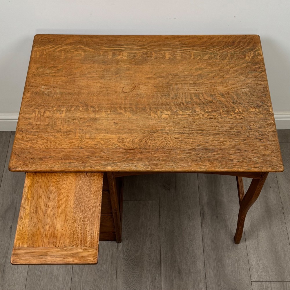 An Edwardian single pedestal oak desk with three stacked drawers on the left, integrated wood pulls, and an open kneehole section supported by slim right-side legs. View X