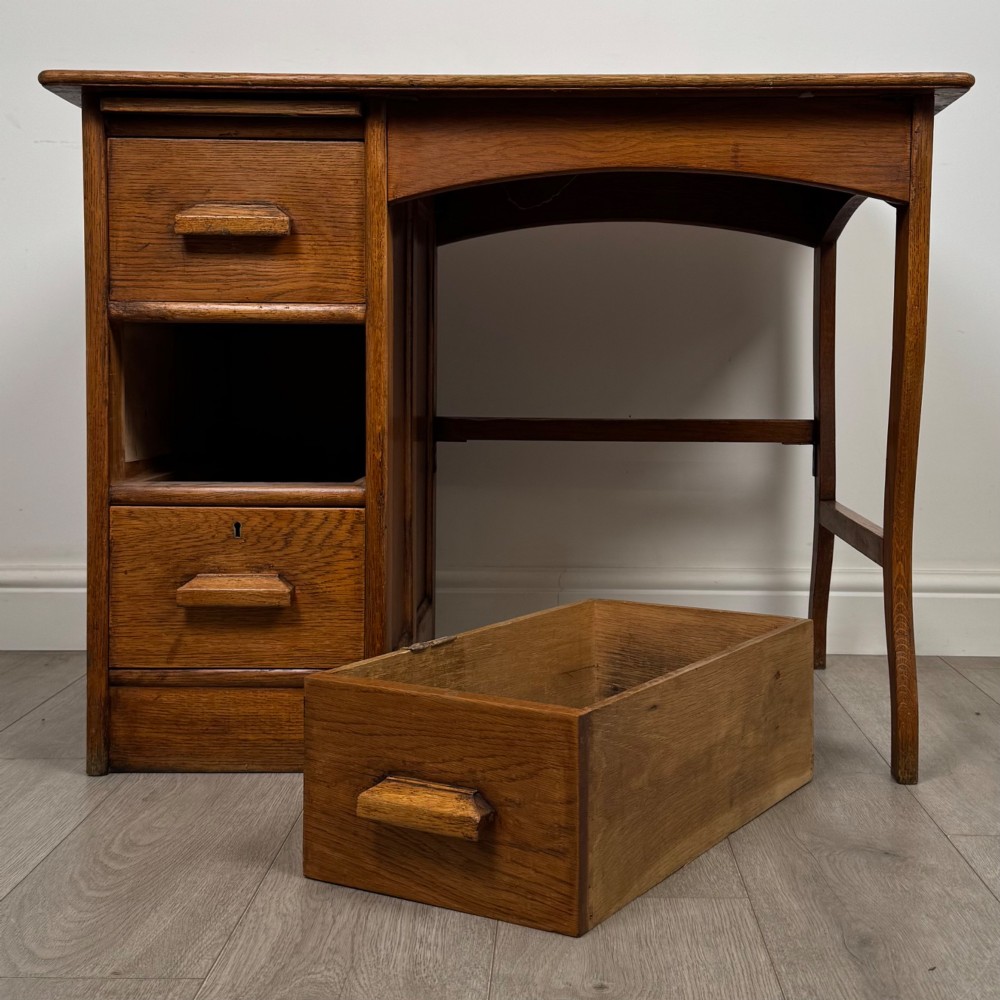 An Edwardian single pedestal oak desk with three stacked drawers on the left, integrated wood pulls, and an open kneehole section supported by slim right-side legs. View XI