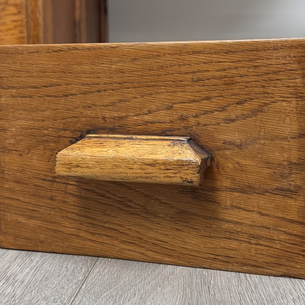 An Edwardian single pedestal oak desk with three stacked drawers on the left, integrated wood pulls, and an open kneehole section supported by slim right-side legs. View XII