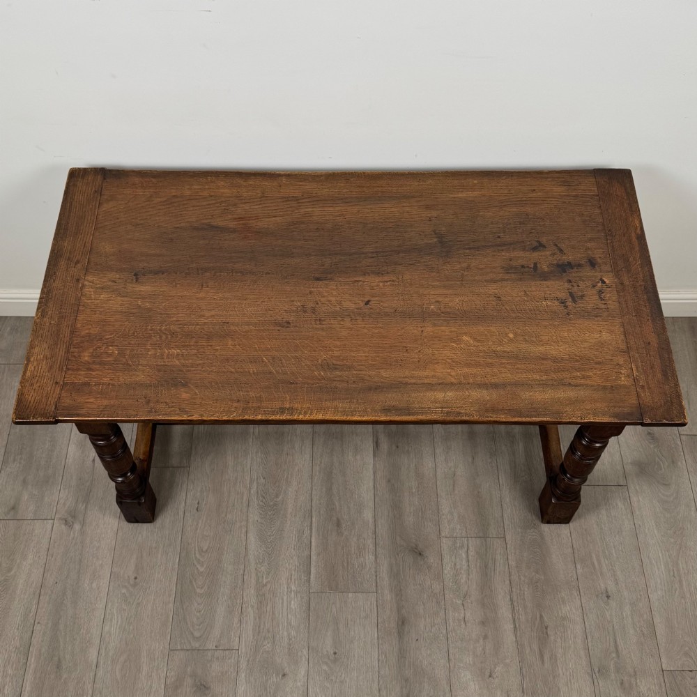 A dark carved oak refectory dining table featuring a carved frieze apron, turned baluster legs, and an H-stretcher base on light timber flooring. View IV
