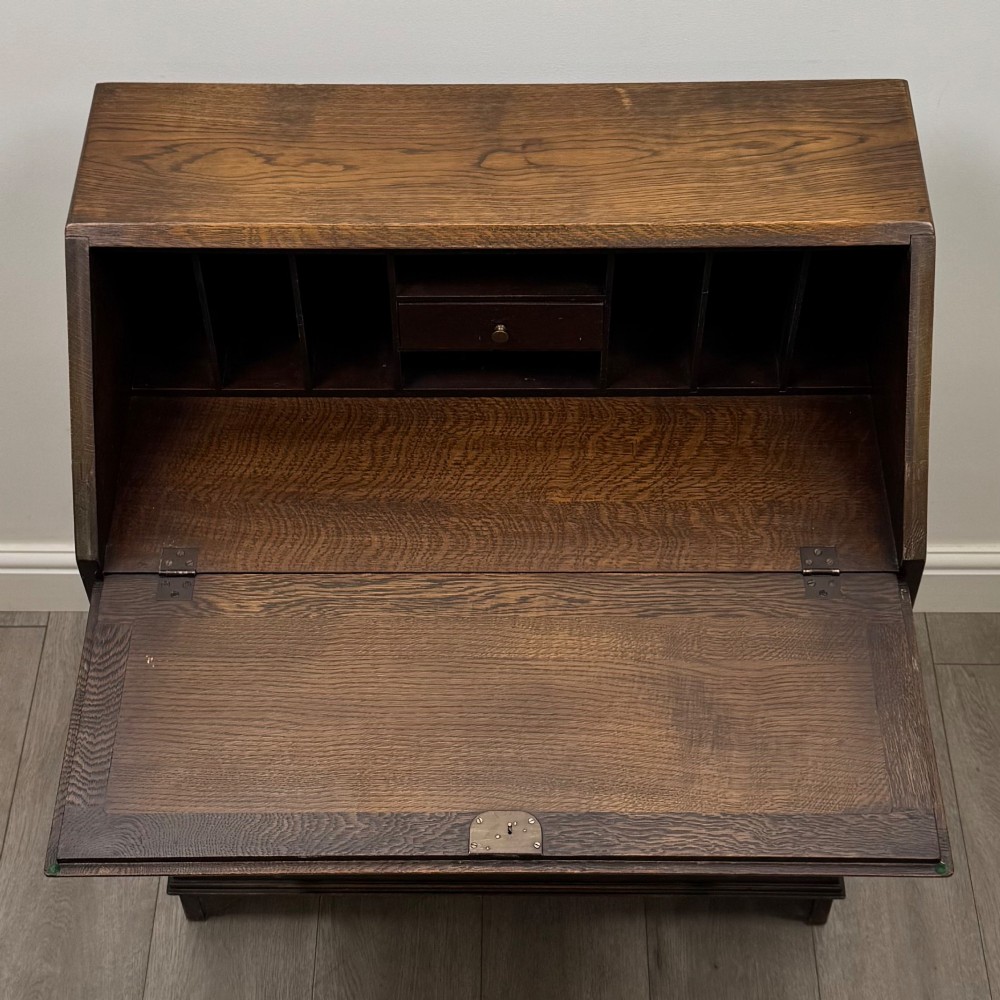 A dark oak writing bureau with a slanted fall-front upper section featuring three carved linenfold panels above four drawers with turned wooden knob handles. View XI