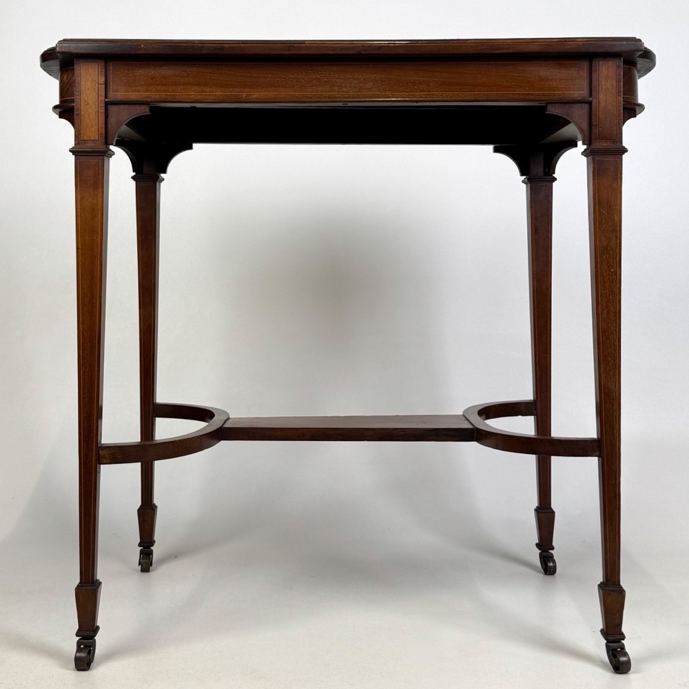 An early 20th-century mahogany side table featuring fine boxwood inlay along the apron, tapered square legs on brass castors, and a curved lower stretcher.