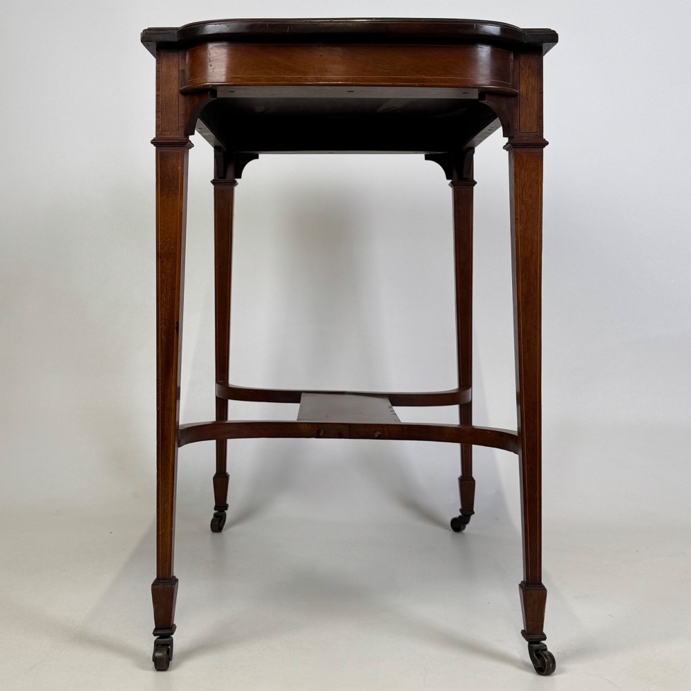 An early 20th-century mahogany side table featuring fine boxwood inlay along the apron, tapered square legs on brass castors, and a curved lower stretcher. View III