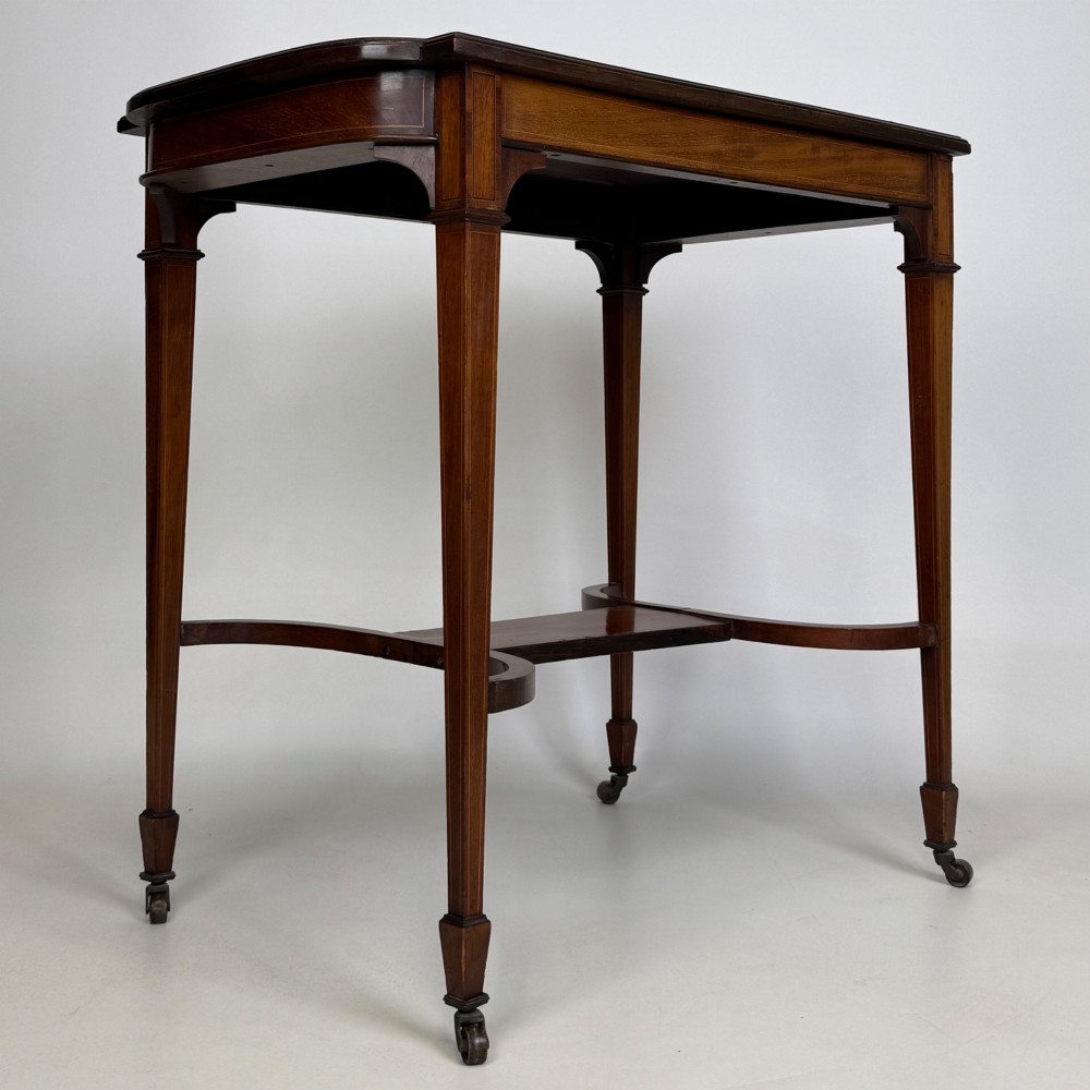 An early 20th-century mahogany side table featuring fine boxwood inlay along the apron, tapered square legs on brass castors, and a curved lower stretcher. View IV