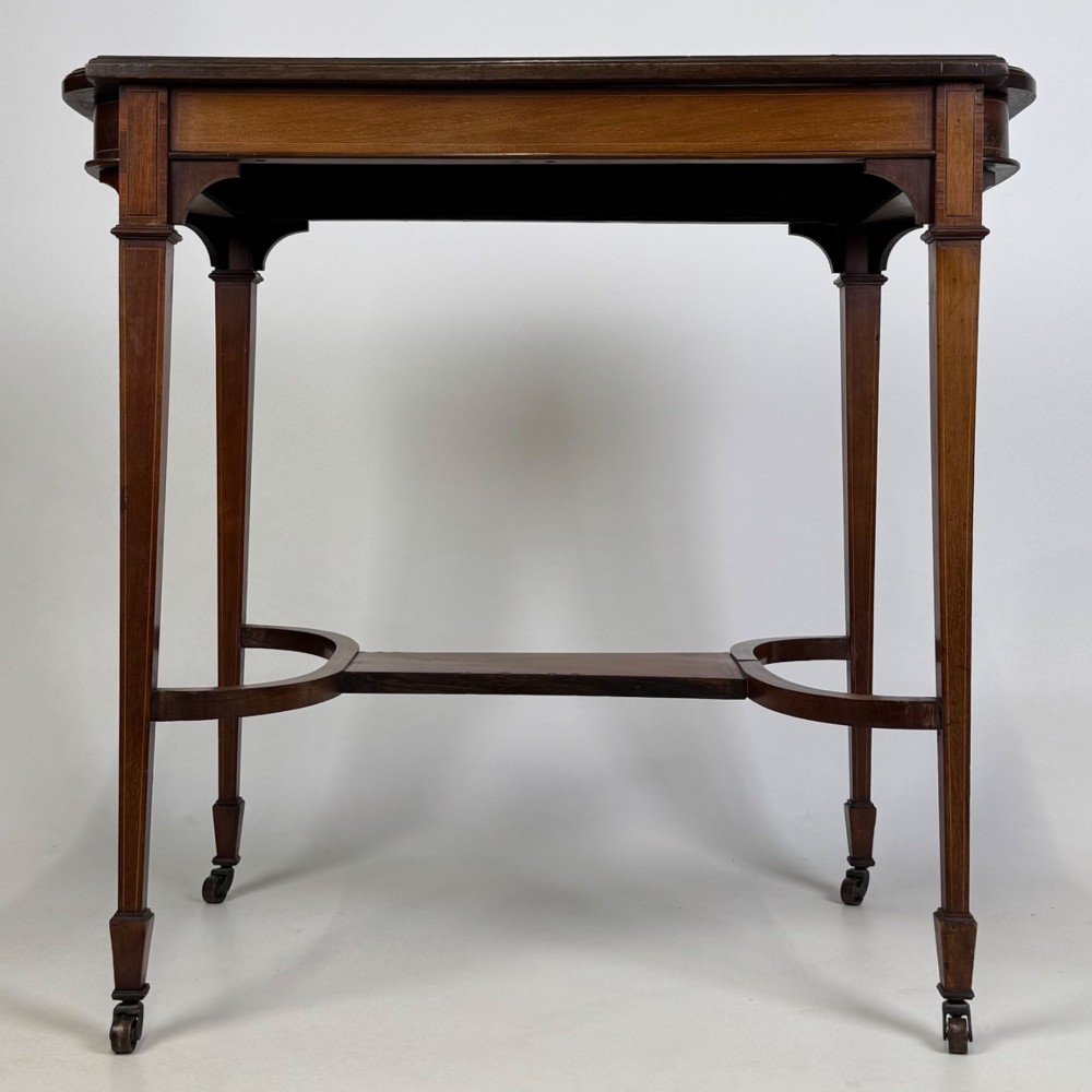 An early 20th-century mahogany side table featuring fine boxwood inlay along the apron, tapered square legs on brass castors, and a curved lower stretcher. View V