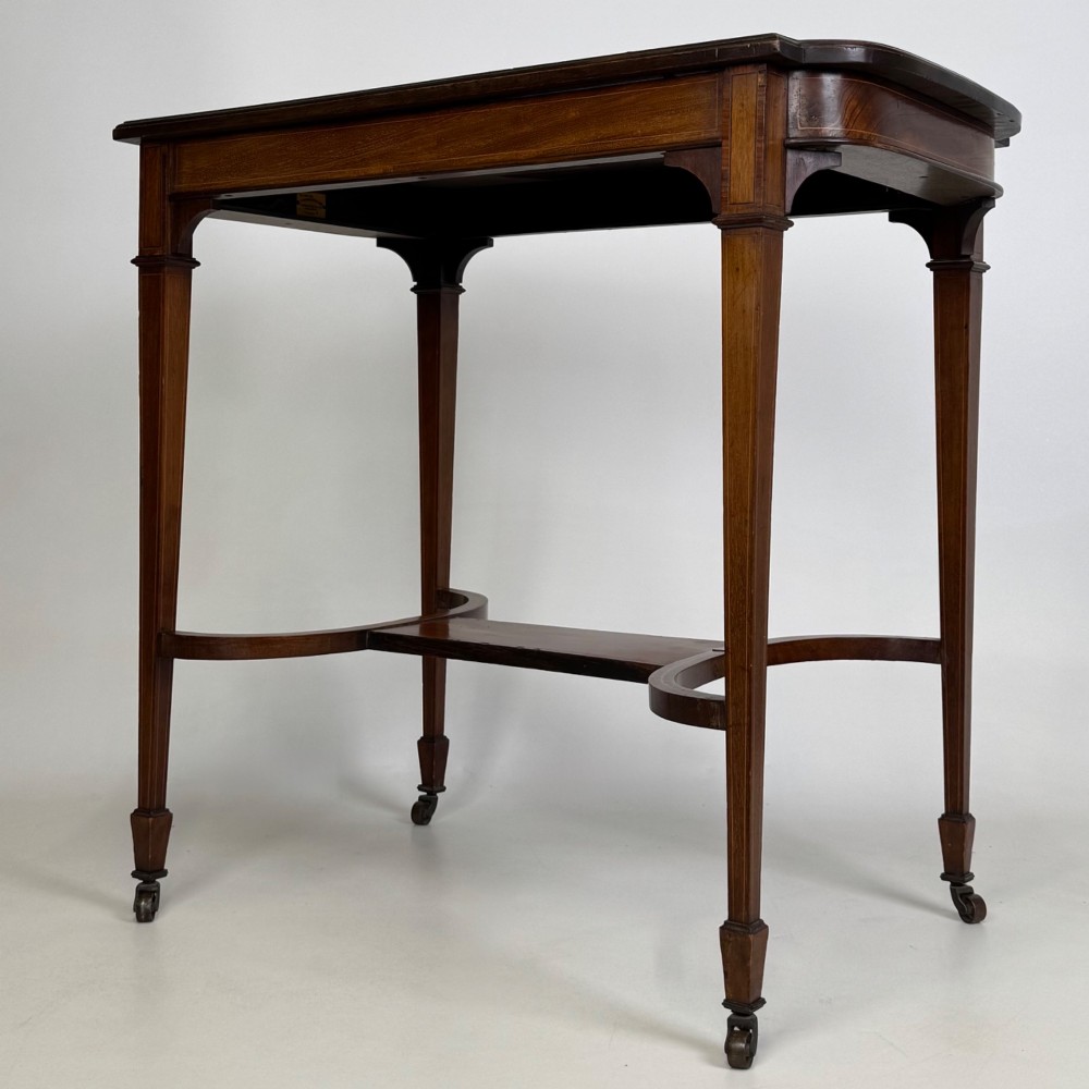 An early 20th-century mahogany side table featuring fine boxwood inlay along the apron, tapered square legs on brass castors, and a curved lower stretcher. View VI