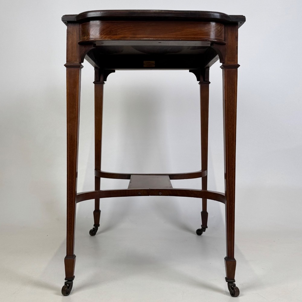 An early 20th-century mahogany side table featuring fine boxwood inlay along the apron, tapered square legs on brass castors, and a curved lower stretcher. View VII