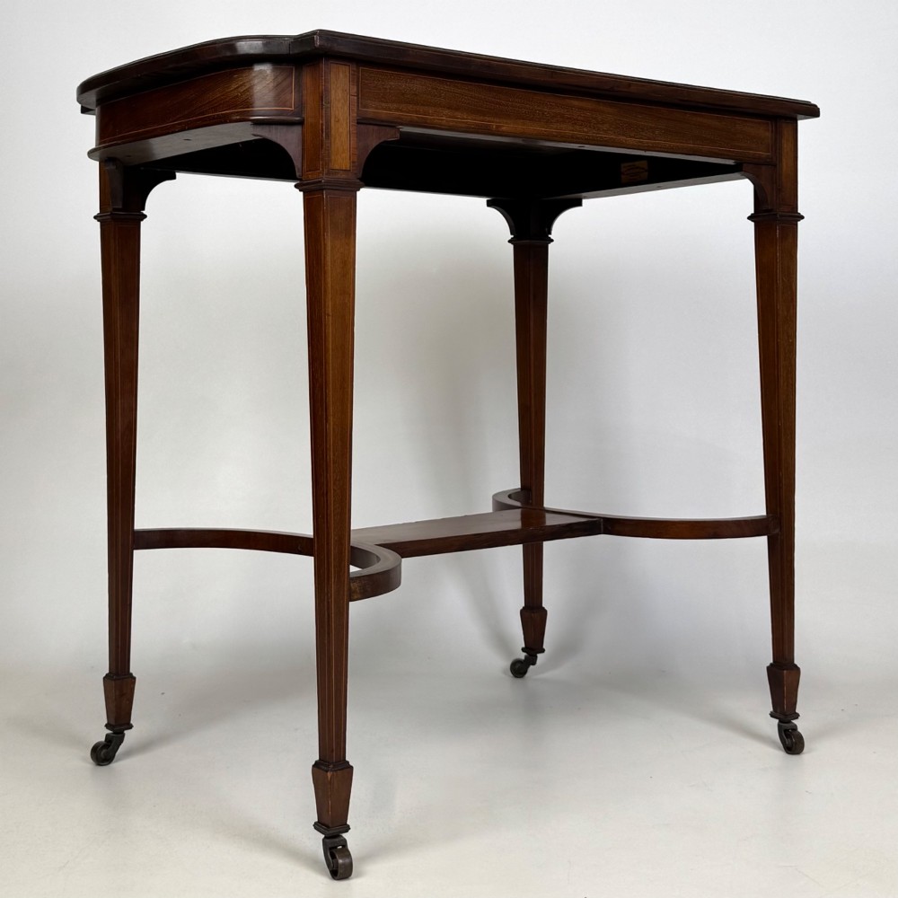 An early 20th-century mahogany side table featuring fine boxwood inlay along the apron, tapered square legs on brass castors, and a curved lower stretcher. View VIII