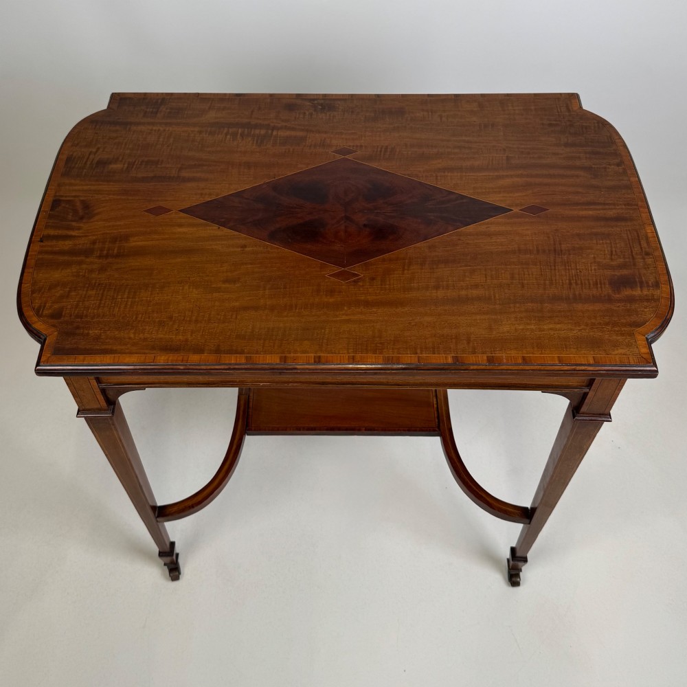 An early 20th-century mahogany side table featuring fine boxwood inlay along the apron, tapered square legs on brass castors, and a curved lower stretcher. View IX